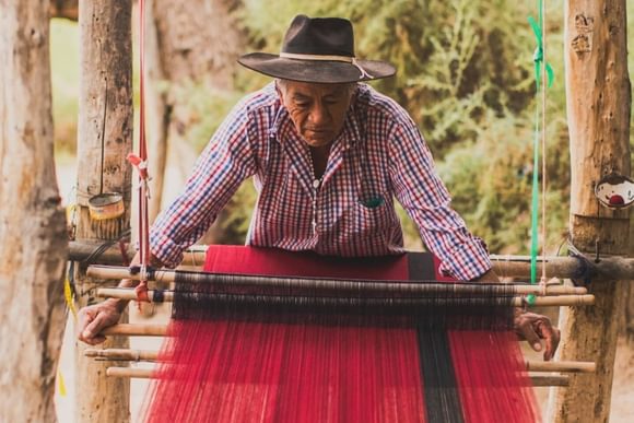 an elderly man weaves on a traditional loom