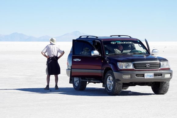 man surveying the vast whiteness of the uyuni salt flat next to a toyota land cruiser 4x4