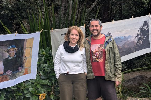 a male and female guide smile in front of a series of photos printed on cloth hung on a clothesline