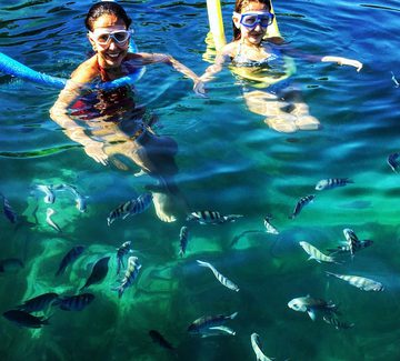 two girls smile for the camera next to colourful fish in the sea