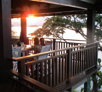 children sitting on a wooden terrace overlooking the sea at sunset