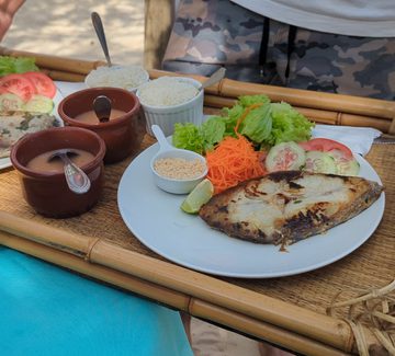 a waitor serves two plates of grilled fish and salad on a beach near paraty