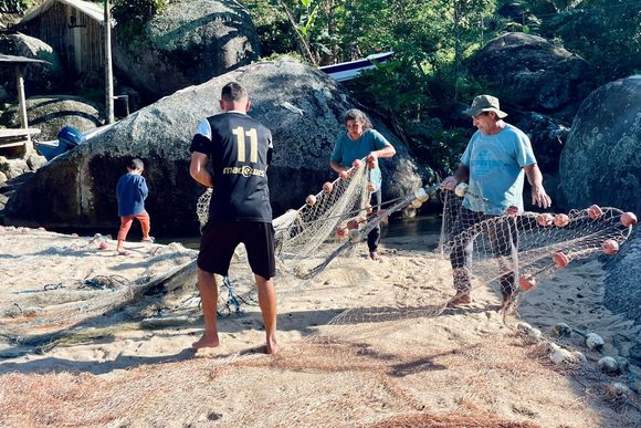a group of locals untangle a fishing net on ponta negra beach