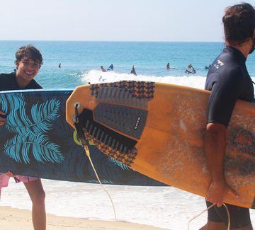 teenage boy smiling with a surfboard in hand on a beach in rio de janeiro