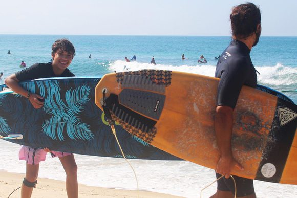 teenage boy smiling with a surfboard in hand on a beach in rio de janeiro