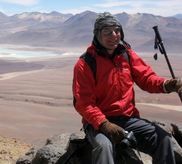 a guide in a red top smiles for the camera on top of the toco volcano in the atacama desert