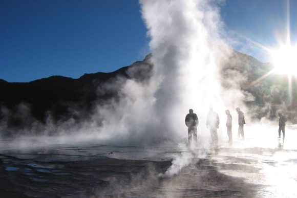 a small group of visitors walk amid the el tatio geysers in the morning light