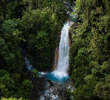 a silvery waterfall drops into a blue pool of water in bajos del toro cloud forest