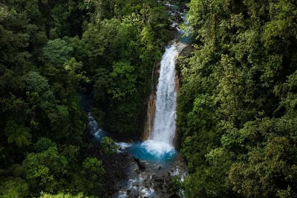 a silvery waterfall drops into a blue pool of water in bajos del toro cloud forest