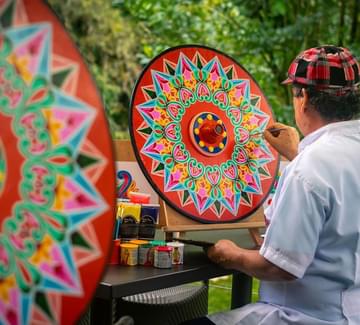 local artist painting a brightly-coloured traditional oxcart wheel in costa rica