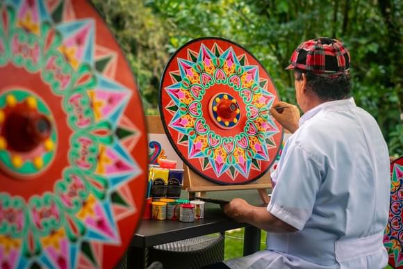 local artist painting a brightly-coloured traditional oxcart wheel in costa rica