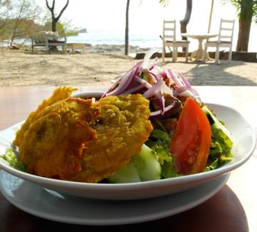 fresh slada and fried fish lunch on a table with a sandy beach in the background