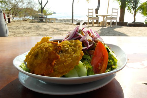fresh slada and fried fish lunch on a table with a sandy beach in the background