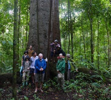 a family with people ranging from children to grandparents pose between a tree with huge butress roots in corcovado national park