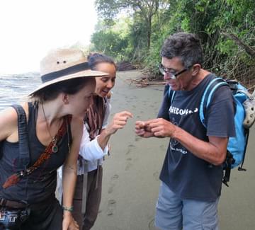 guide showing a hermit crab to two females travellers on a beach on the osa peninsula