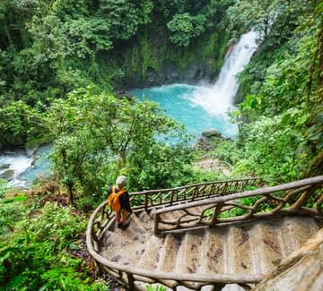 man walking down path towards the bright turquoise waters of rio celeste