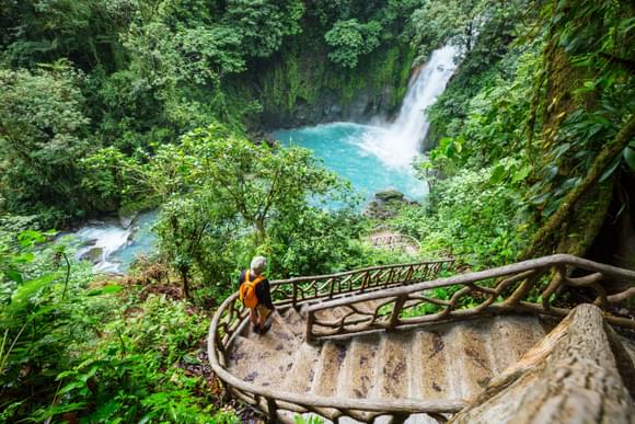 man walking down path towards the bright turquoise waters of rio celeste