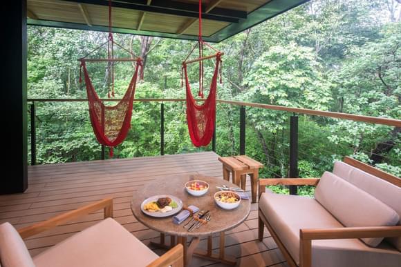 hammocks strung up on a hotel terrace with fresh food on the table in the foreground
