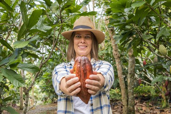 smiling lady holds out a cacao fruit