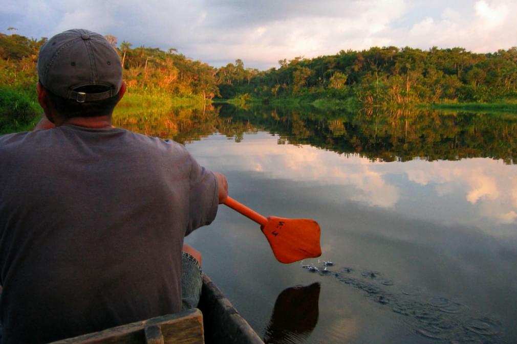 Ecuador amazon napo wildlife centre man paddling across black water lagoon red oar flip